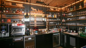 Eine Bar mit Regalen voller Flaschen und Gläsern, einer Kaffeemaschine und einem Schild, das die angebotenen Weinsorten ausweist.