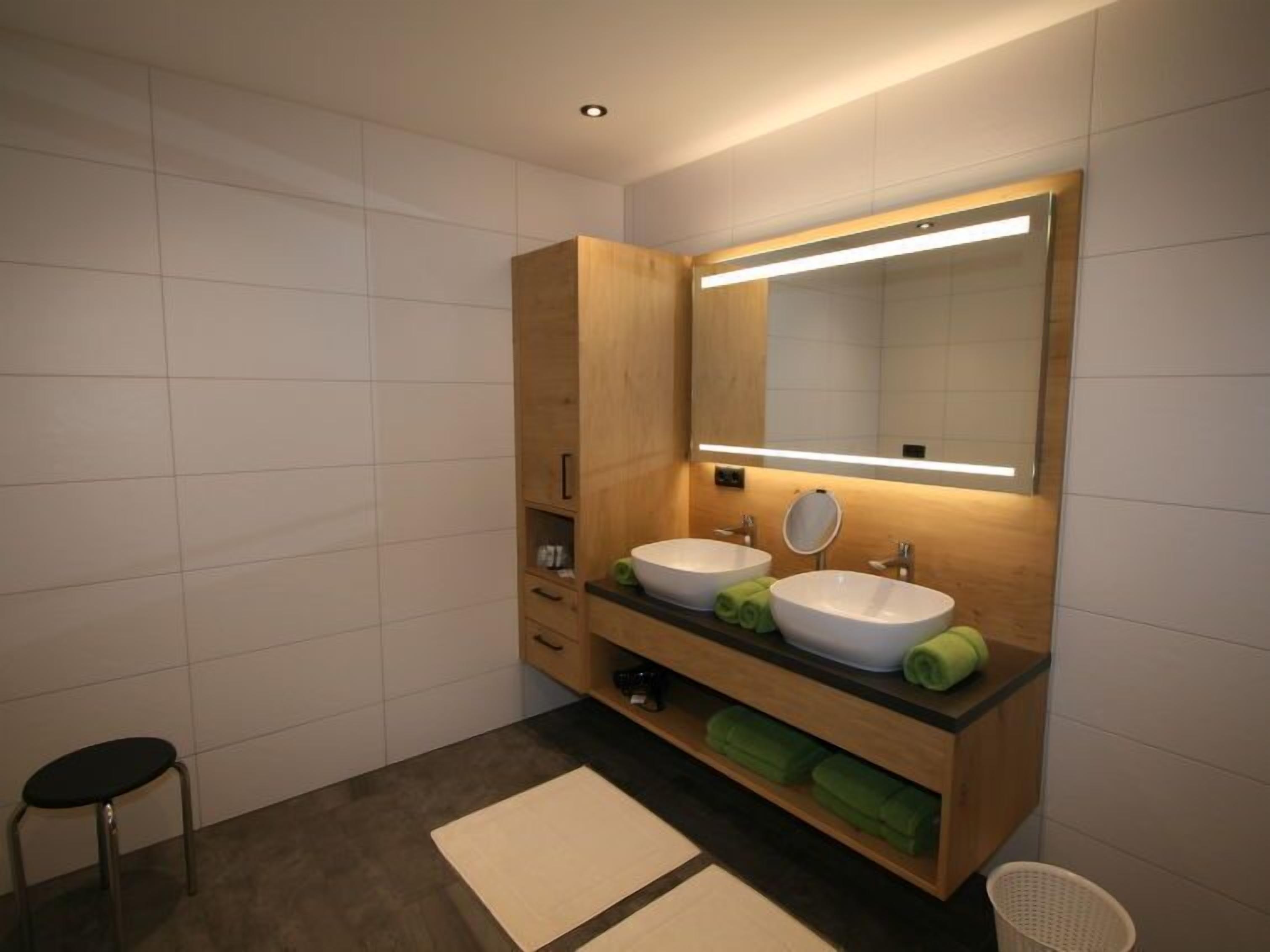 A modern bathroom with two sinks, a mirror, and wooden cabinetry.