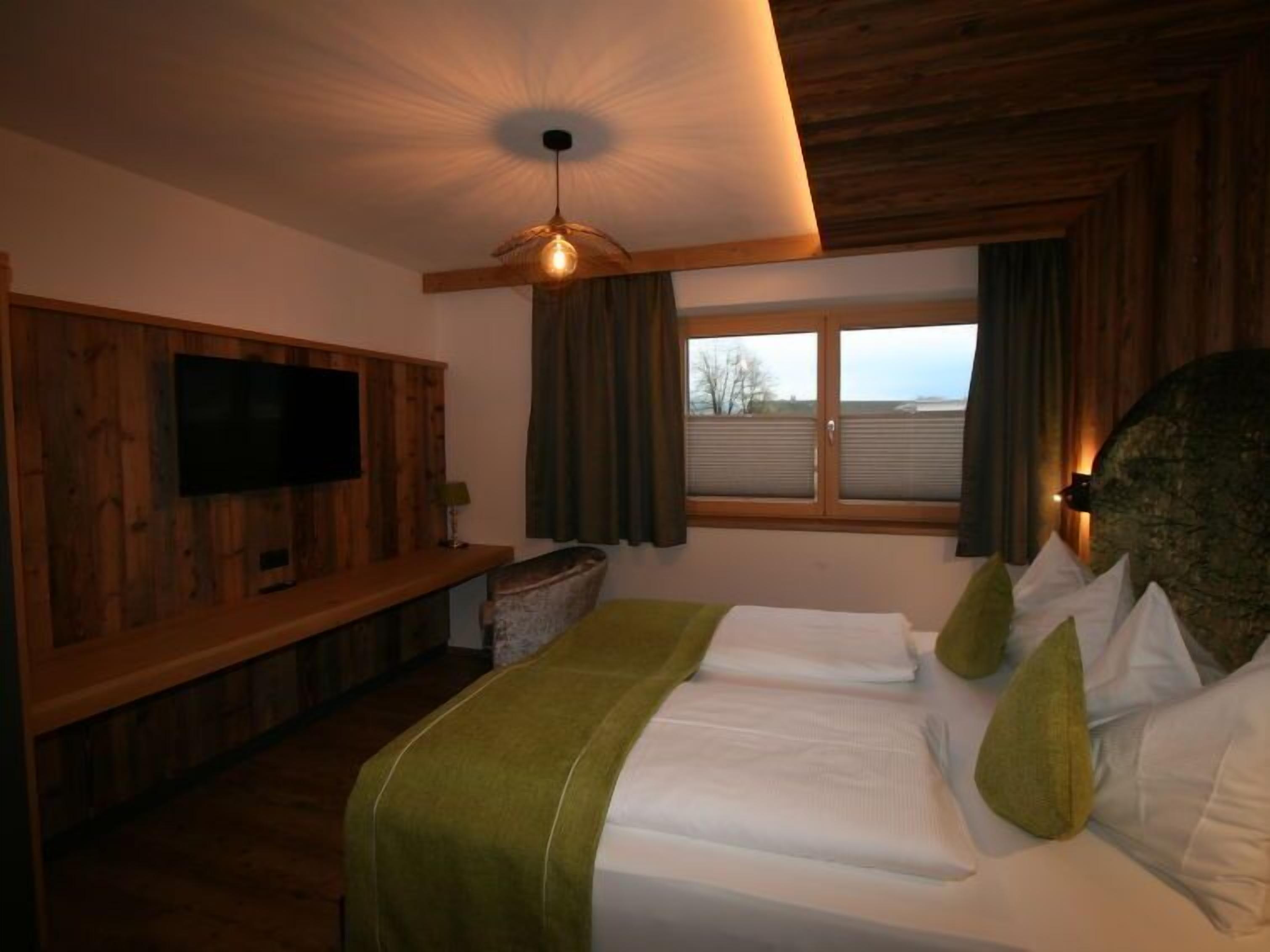 Habitación de hotel con techo de madera, televisor montado en la pared, ventana grande con cortinas y cama con almohadas.