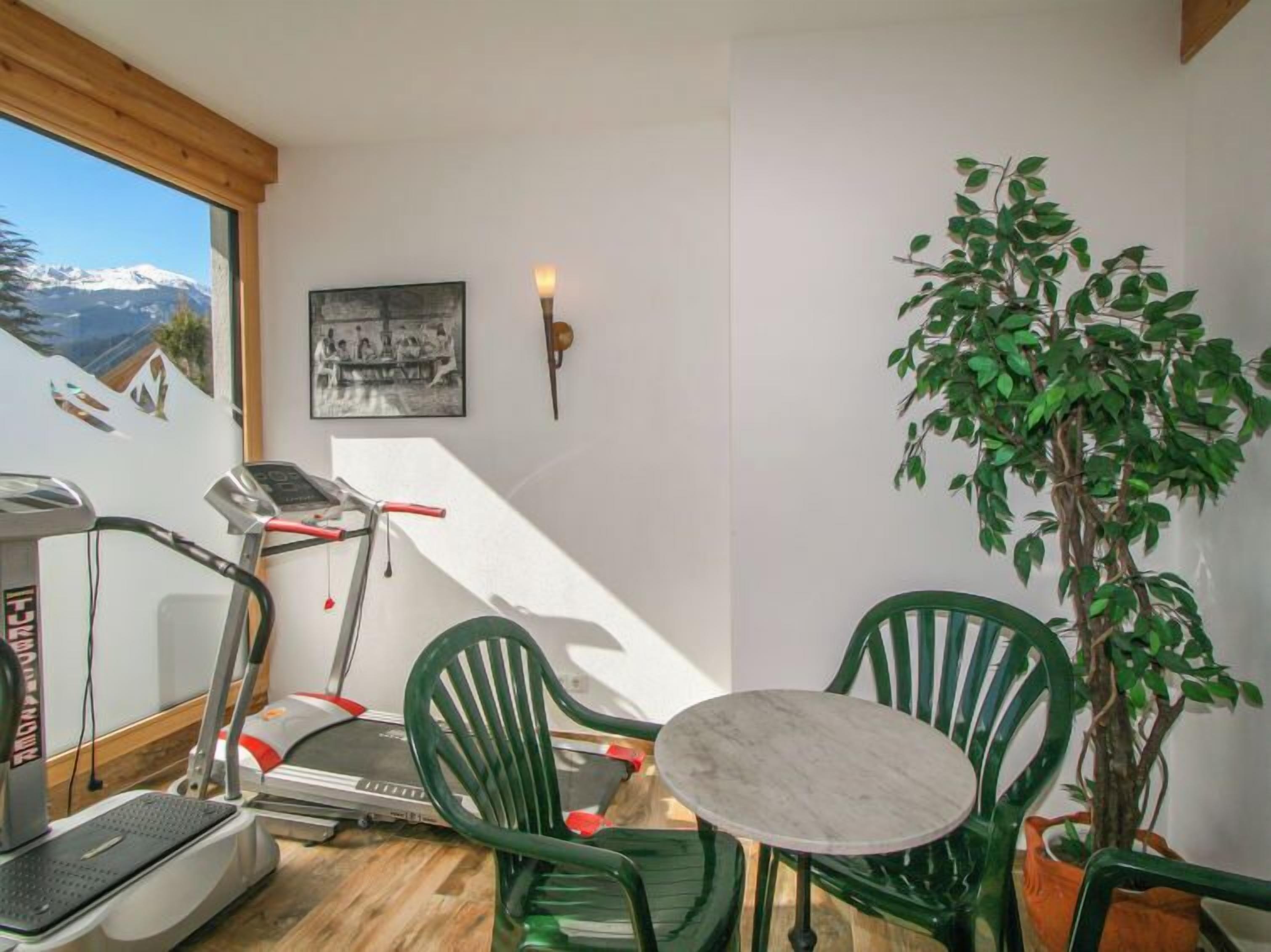 Une pièce équipée d’un tapis de course, de chaises vertes, d’une petite table et d’une plante en pot.