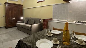 Un comedor con una mesa dispuesta para cuatro personas, un sofá, un armario y una cocina al fondo.