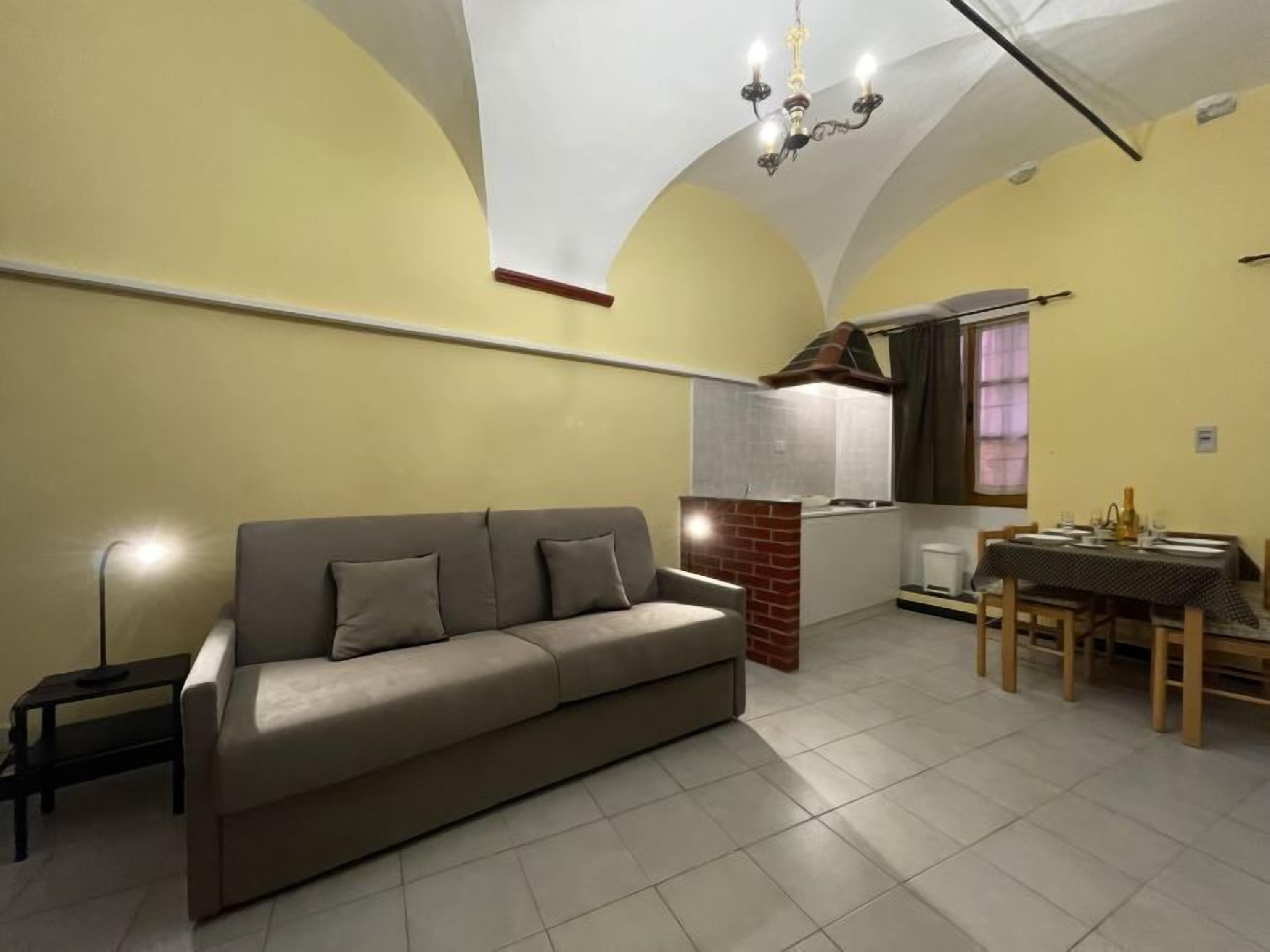 Ein Wohnzimmer mit einer Couch, einem Esstisch mit Stühlen, einer Küchenzeile und einem Kronleuchter.