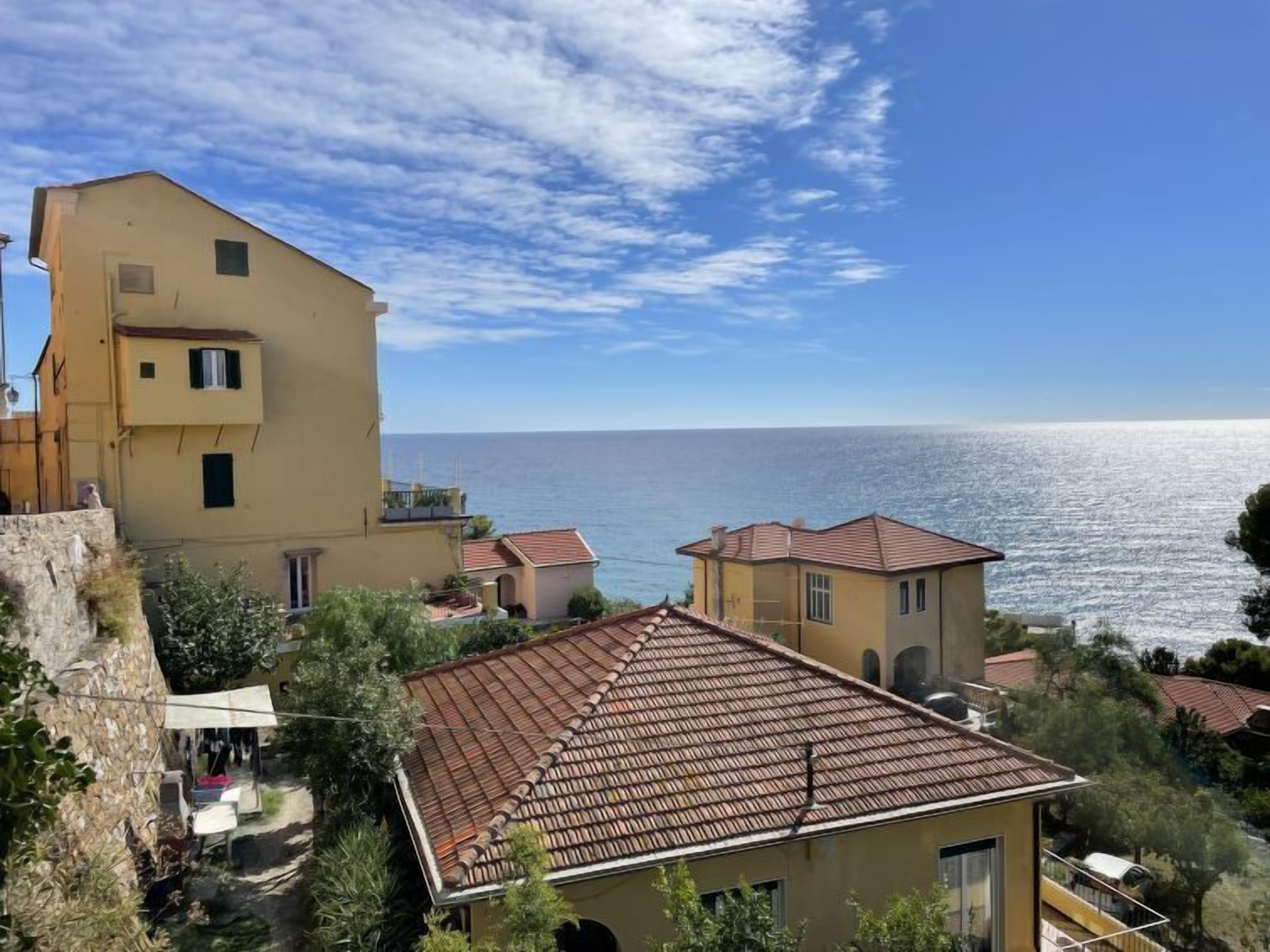 A coastal building with a tiled roof, a stone wall, and a view of the sea.