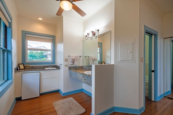 A modern bathroom with a window, a ceiling fan, a sink, a mirror, and a door.