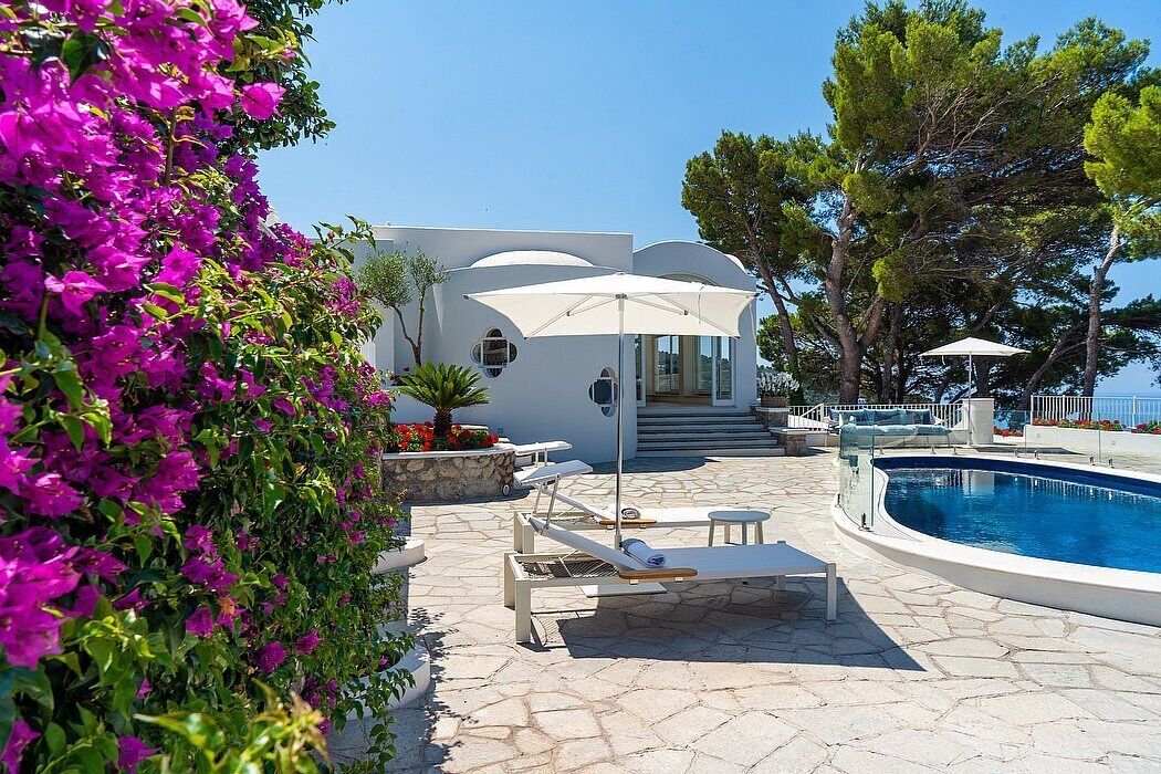 Un espace aménagé au bord de la piscine, avec des chaises longues, un parasol blanc et une piscine.