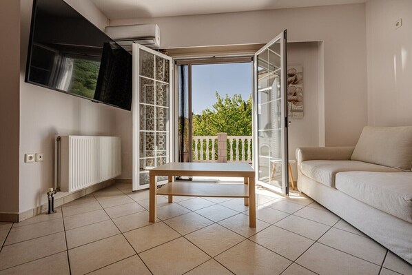 A living room with a white sofa, a wooden table, and a sliding glass door leading to a balcony with a white railing.