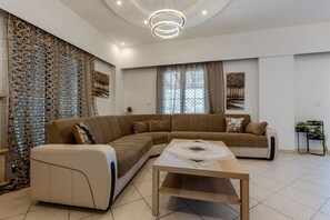 A modern living room with a sectional sofa, a coffee table, decorative curtains, and a chandelier.