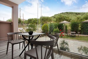 An outdoor patio with a table and chairs, surrounded by greenery and a view of a hilly landscape.