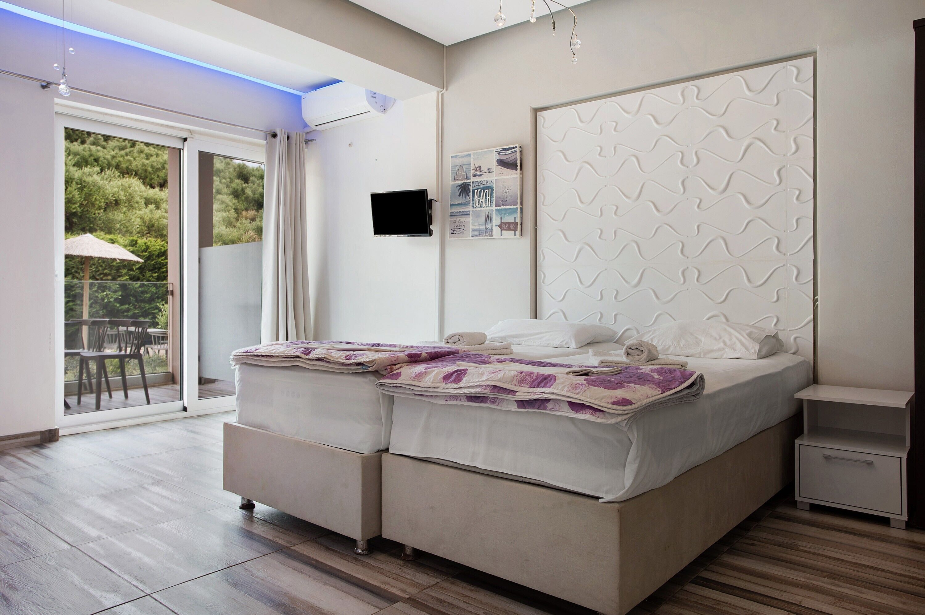 Un dormitorio con una cama, un televisor, un estante en la pared y un ventanal corredizo a un balcón.