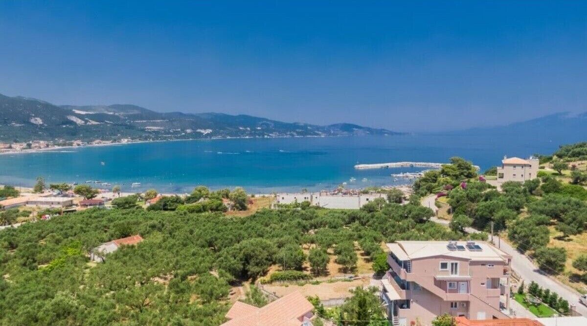 A coastal view with a building surrounded by greenery and a clear blue sea.