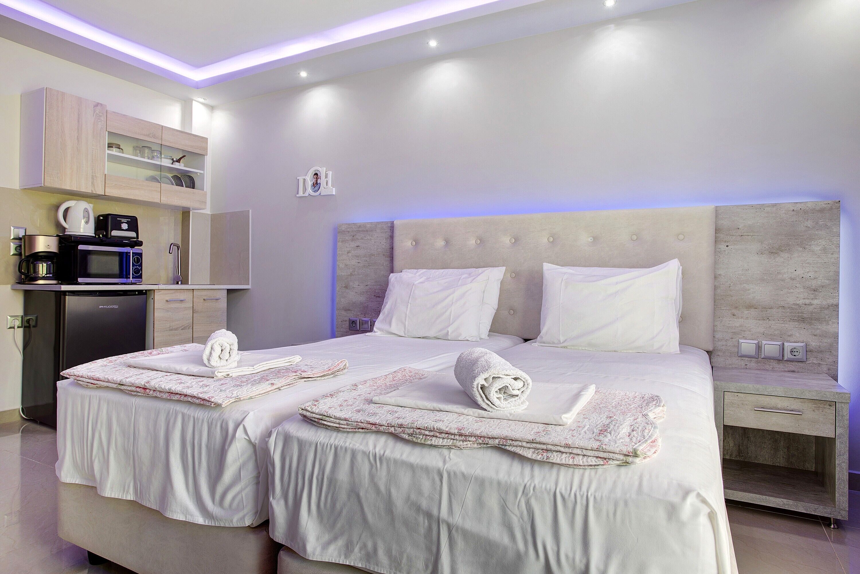 A hotel room with two beds, a kitchenette, and a bedside table.