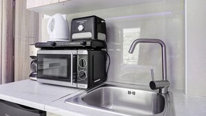 Eine Küche mit Mikrowelle, Toaster und Kaffeemaschine auf der Arbeitsfläche, einem Edelstahlspülbecken und Holzschränken.