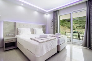 A modern bedroom with a large bed, a nightstand, and a view of a balcony with outdoor furniture.