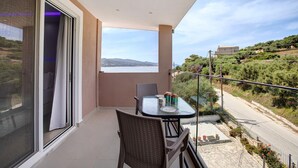 Un balcón con mesa y sillas, vista al mar y una ladera.