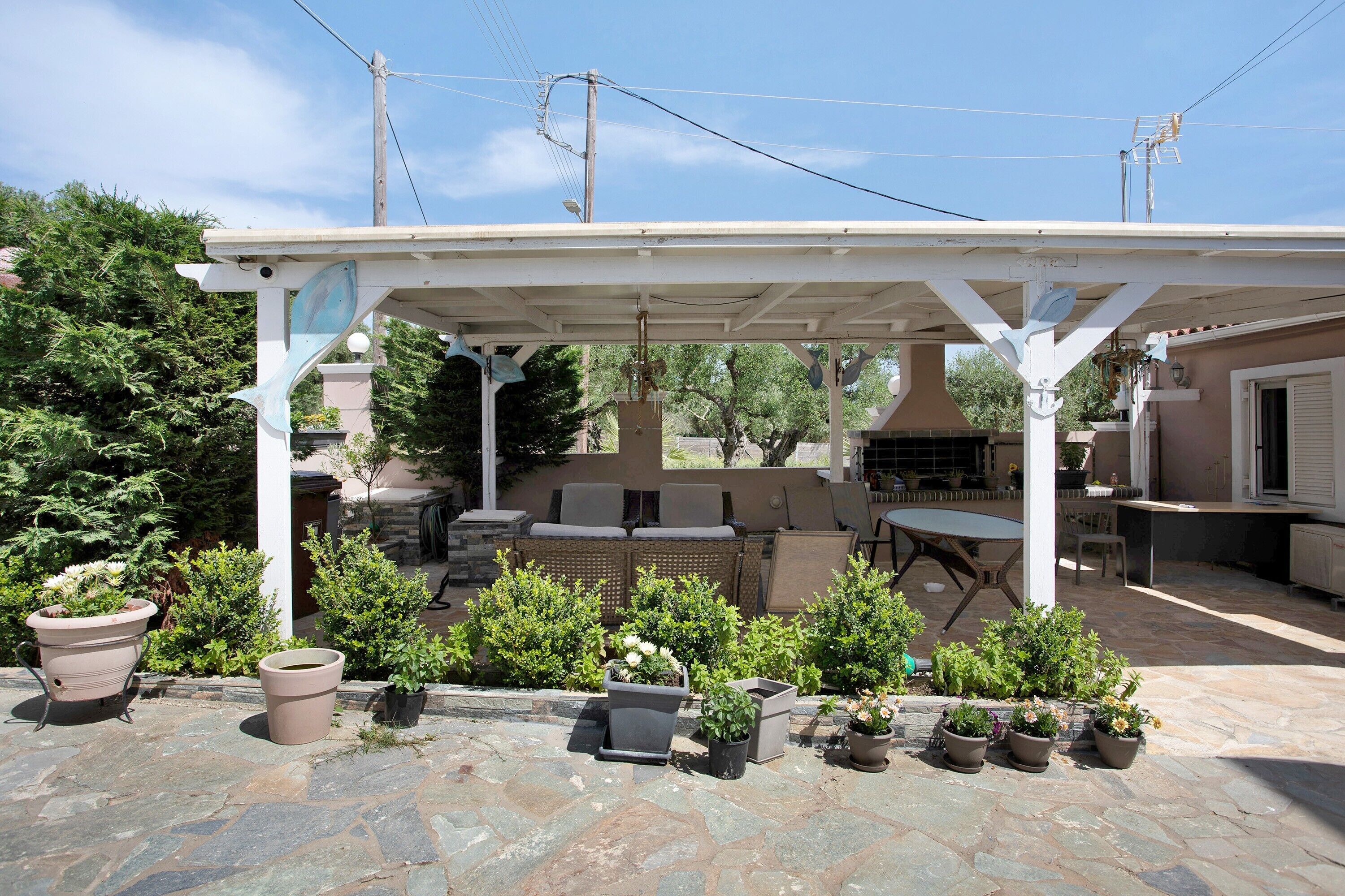 Un patio couvert avec des meubles d’extérieur, un barbecue et des plantes en pot.