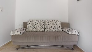 Um sofá em tons neutros com almofadas estampadas, estrutura metálica e parede lisa com interruptor e tomada.