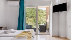 Quarto de hotel com cama, televisão, varanda e vista para o verde, além de porta de correr.