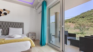 Quarto com cama, mesa de cabeceira e porta de vidro que dá para uma varanda com mobiliário exterior.