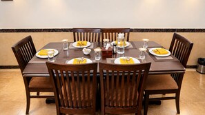 A dining table set for six with chairs, plates, cutlery, and glasses.
