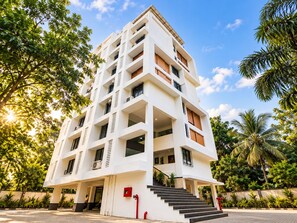 A multi-story building with a central staircase, surrounded by lush greenery and palm trees.