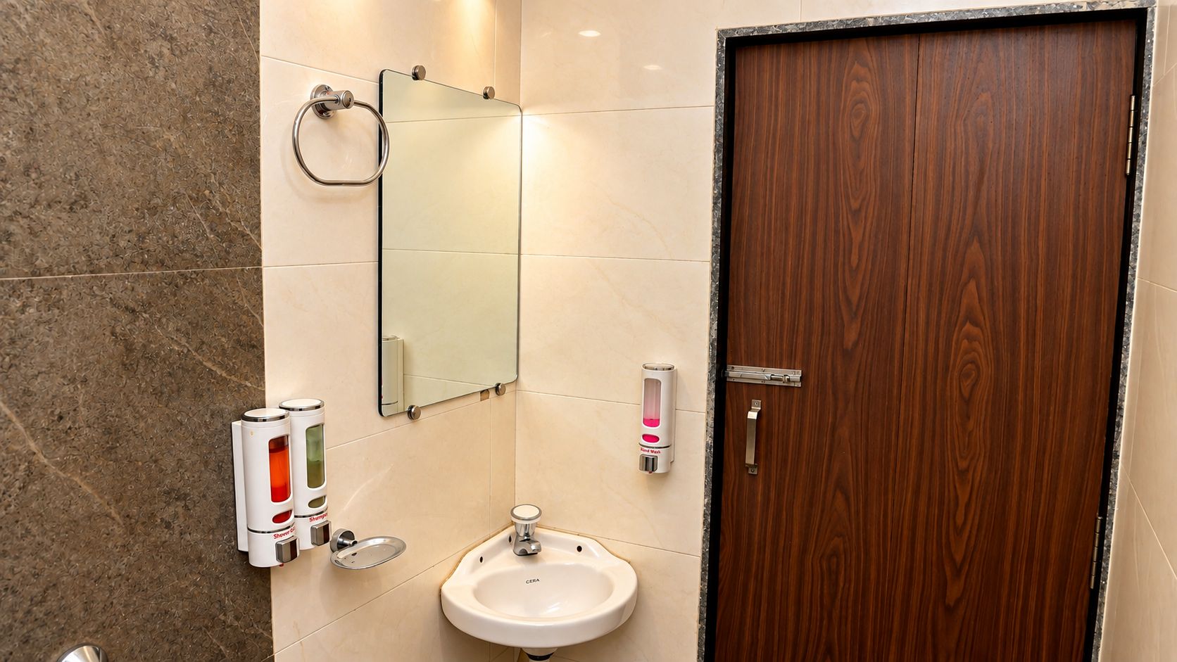 Une salle de bain avec une porte en bois, un miroir, un lavabo et deux distributeurs de savon.