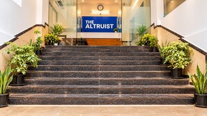 Marmeren trappen leiden naar een receptiegedeelte met een bordje waarop 'THE ALTRUST' staat.