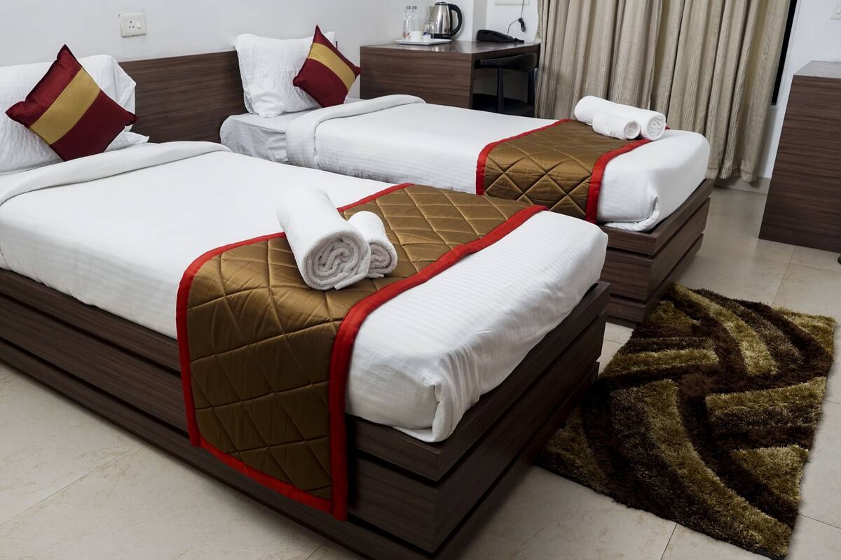 Habitación de hotel con dos camas, cada una con cabecero marrón y ropa de cama blanca. Hay una mesita con un hervidor y una taza, y un bote de basura en la esquina.