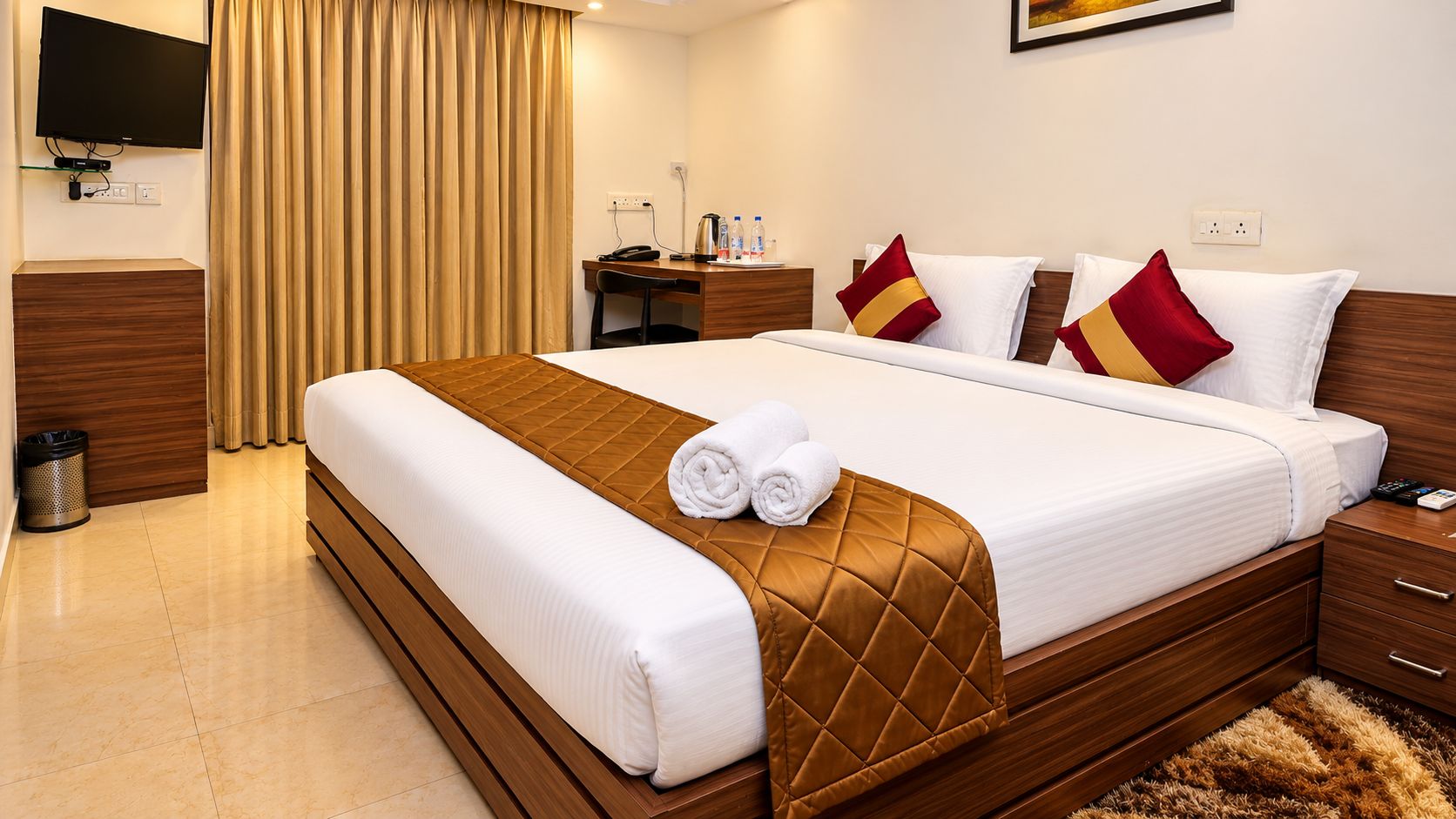 A hotel room with a large bed, a desk, a chair, a TV, and a trash bin.