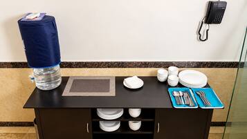 Zona de recepción de un hotel con dispensador de agua, un teléfono y una mesa preparada con platos, tazones y cubiertos.