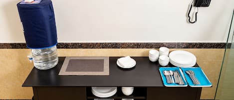 Zona de recepción de un hotel con dispensador de agua, un teléfono y una mesa preparada con platos, tazones y cubiertos.