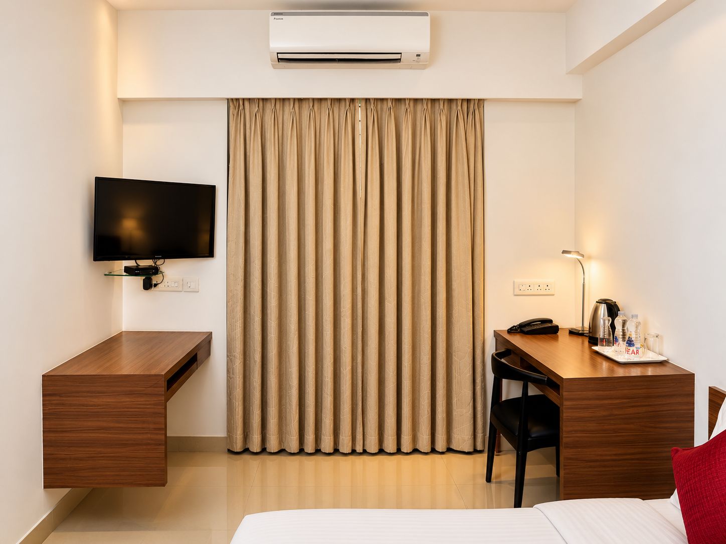 A hotel room with a bed, a desk, a chair, a television, an air conditioner, and a curtain.
