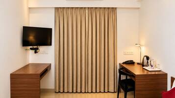 A hotel room with a bed, a desk, a chair, a television, an air conditioner, and a curtain.