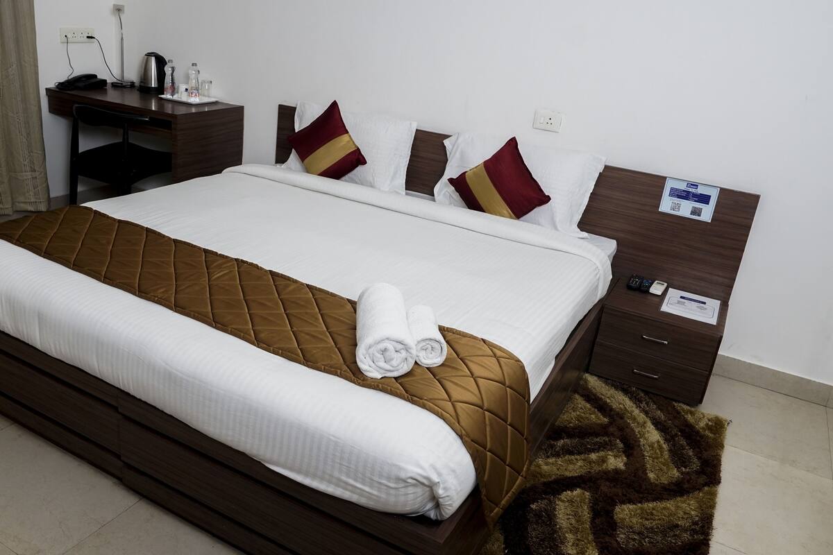 Habitación de hotel con una cama grande, un escritorio con silla, una cafetera y una mesita de noche con teléfono y placa de identificación.