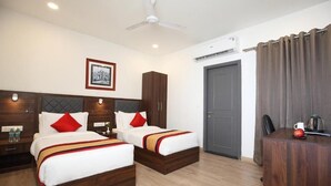 Habitación de hotel con dos camas, un escritorio, una silla, un ventilador de techo y un equipo de aire acondicionado, además de una puerta.