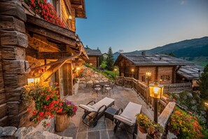 A log cabin with a stone patio, outdoor seating, and a view of the mountains.
