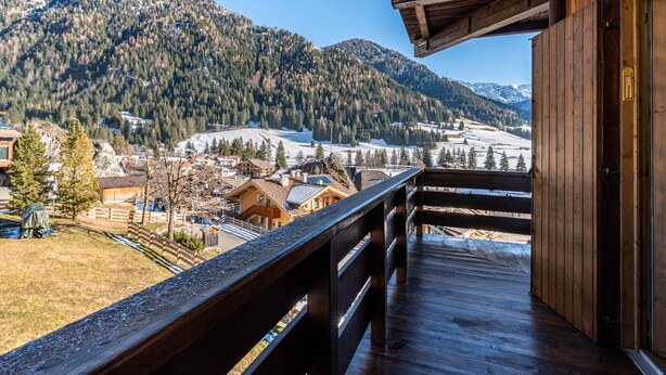 A wooden balcony with a view of a mountainous landscape and a village below.