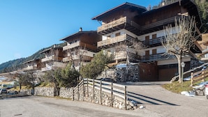 A traditional chalet-style building with multiple balconies, stone walls, and a paved driveway.