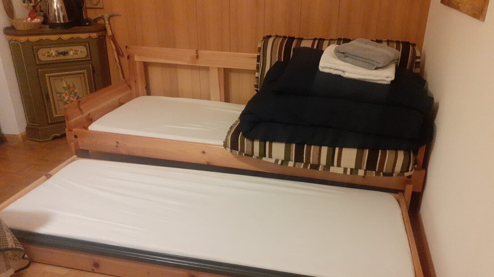 A double bed with wooden headboard and footboard, a small bedside table with a lamp, and a striped cushion.