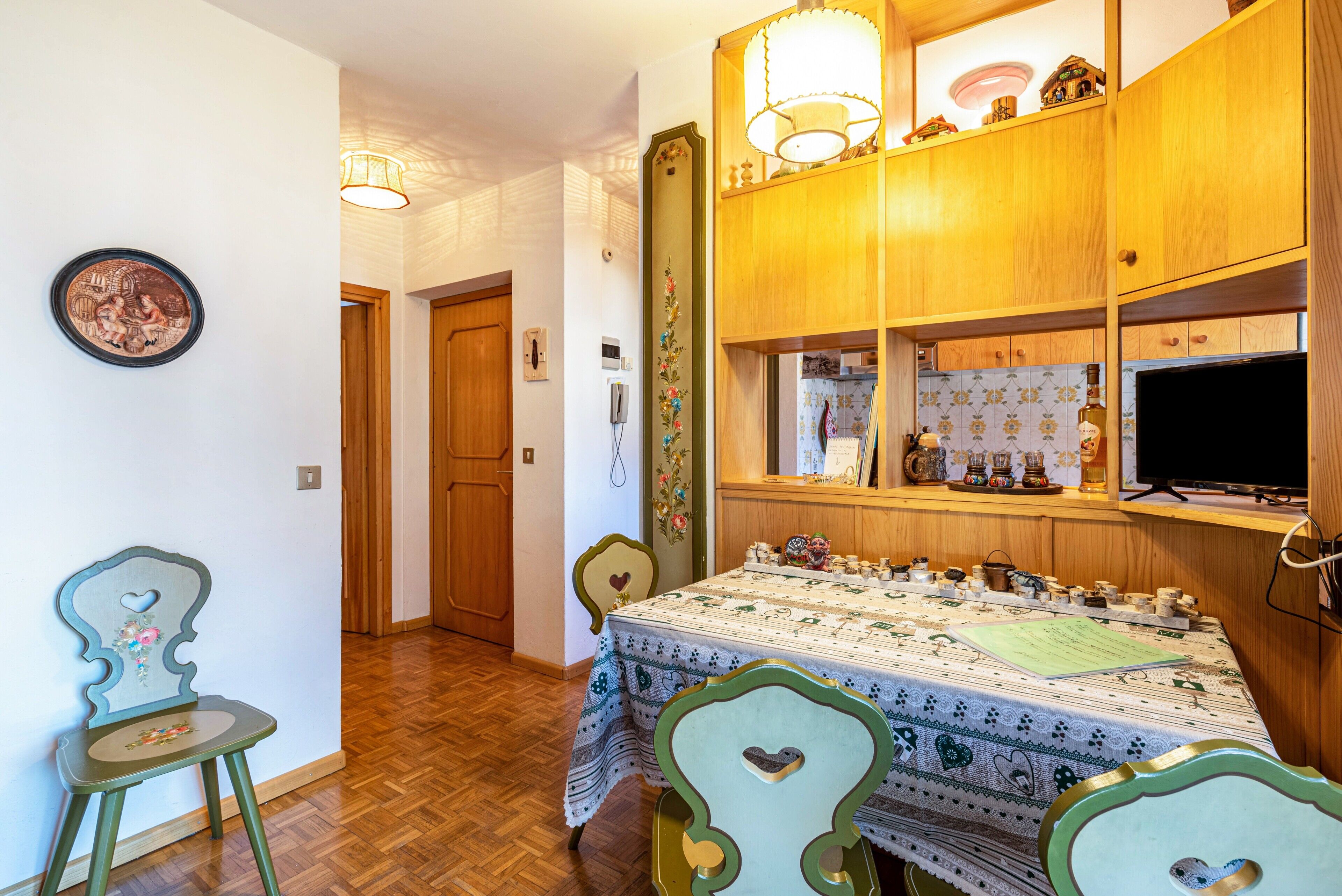 A dining area with a table set for four, wooden cabinets above, and a hallway leading to another room.