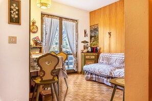 Une pièce comprenant un lit, une chaise, une table, un radiateur, une fenêtre avec des rideaux et un mur orné d’une horloge et d’un tableau.