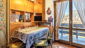 A dining area with a table set for two, wooden cabinets, a television, and a view through a large window.