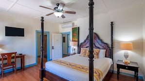 A four-poster bed with a wooden headboard, a ceiling fan, a bedside table with a lamp, and a television on the wall.