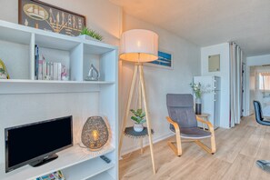 A modern living room with a flat-screen TV, a floor lamp, a bookshelf, and a chair. - Sea View Apartment Arcachon – Private Terrace & Balcony, Sleeps 4 (Arcachon)