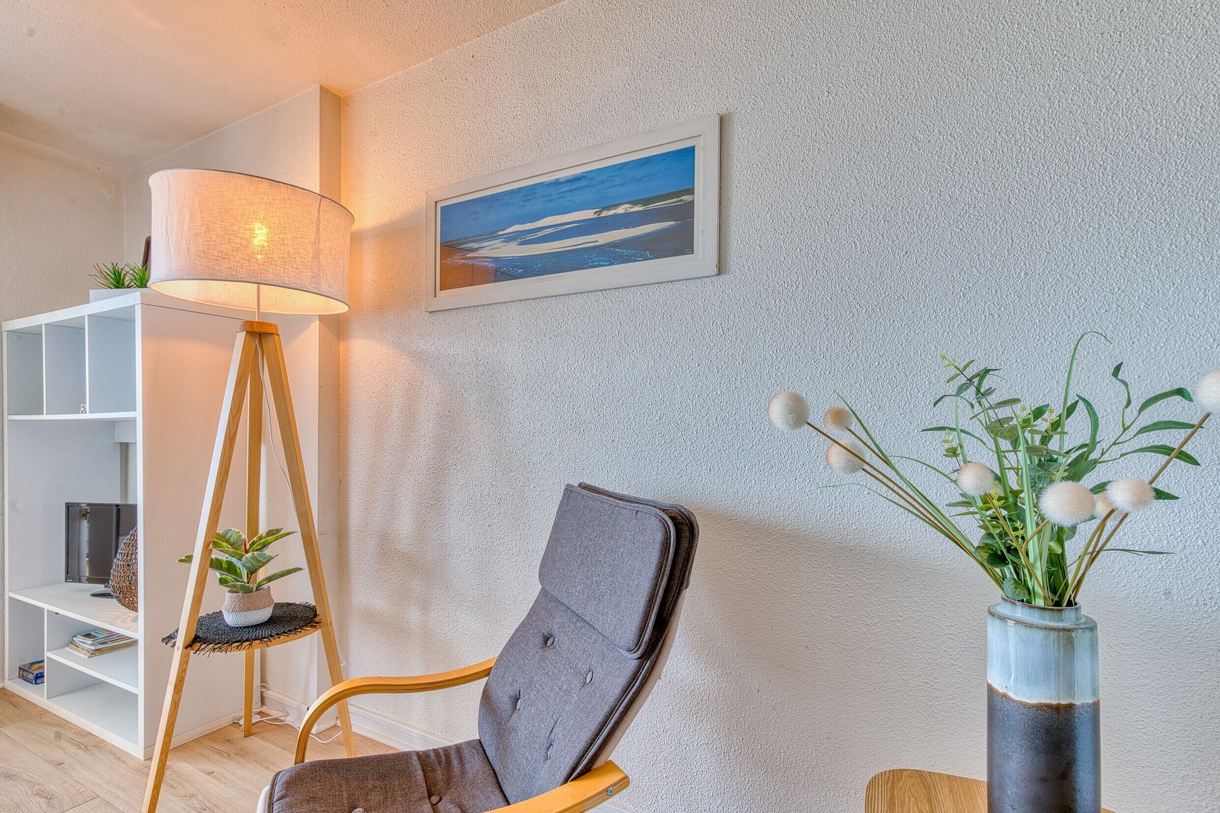 Un soggiorno moderno con una lampada da terra, una poltrona, una libreria, un quadro incorniciato e un vaso con piante.