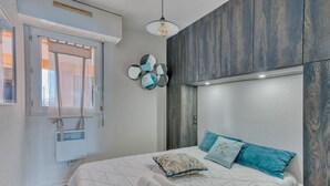 Ein Schlafzimmer mit einem Bett, einem Fenster mit Vorhängen, einem Wandheizkörper und einer Deckenleuchte.