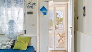 Quarto com cama, travesseiro verde, colcha azul, porta branca e vista para o exterior.