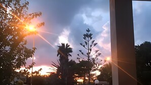 Vista do pôr do sol de uma área externa coberta, com portão e árvores.