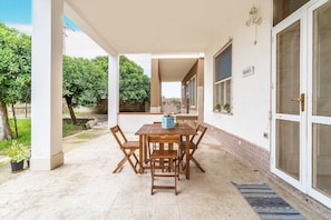 Un patio al aire libre con mesa y sillas de madera, piso de baldosas y una puerta con un letrero.