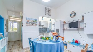 Cozinha compacta com área de refeições, um relógio e uma TV numa estante.