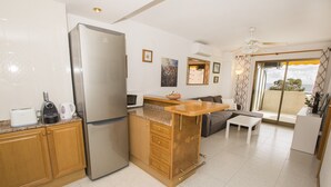A compact kitchen with a refrigerator, microwave, and coffee maker. There is a wooden counter with a sink and a dining area with a sofa and a table. - A102 CALPPLACE 2-5º-2 (Calpe)
